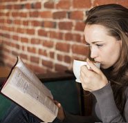 Does God exist - Photo of a young woman, drinking a cup of coffee and reading the Bible, to learn about a relationship with God.