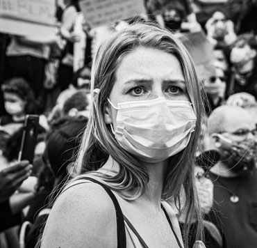 Photo of a woman amid a protest march. She wears a mask due to COVID-19. In this world, there is political unrest and pestilence.